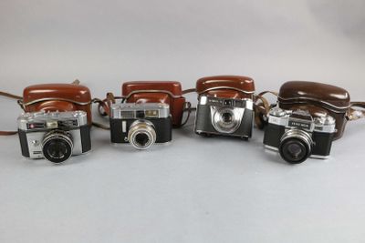 four old cameras are lined up on a white surface