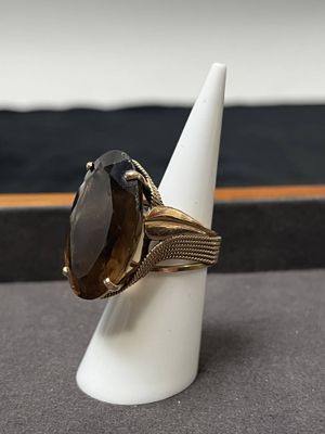 bague en or sertie d'une pierre de smokyite, posée sur un cône blanc, sur une table