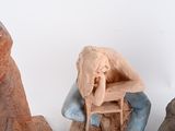 three clay sculptures of a man and a woman sitting on a bench