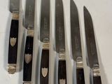 six couteaux sont alignés sur une surface blanche