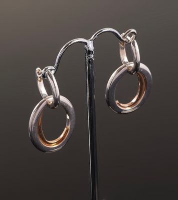 a pair of silver and gold hoop earrings on a black stand
