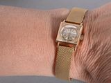 someone is wearing a gold watch on their wrist with a gold band