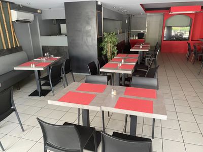 Dans un restaurant aux murs rouges, des tables et des chaises sont alignées.
