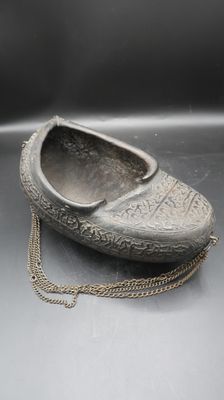 une vieille chaussure en argent à laquelle est suspendue une chaîne sur le côté