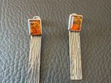 une paire de boucles d'oreilles argentées et orange posées sur une surface en cuir noir