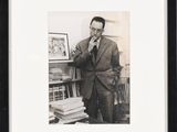 black and white photograph of a man in a suit leaning against a bookshelf
