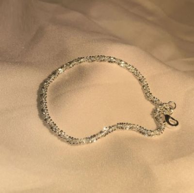 bracelet à chaîne en argent posé sur un lit, avec un drap blanc en arrière-plan