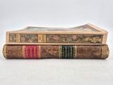 two old books stacked on top of each other on a white surface