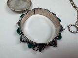 a silver bracelet with a green flower on it next to a chain