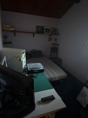 une pièce faiblement éclairée dans laquelle se trouvent un lit, un bureau et une télévision