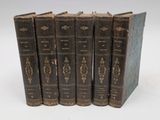 six old books are lined up in a row on a white surface