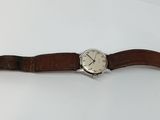 gros plan d'une montre sur une surface blanche avec un bracelet marron