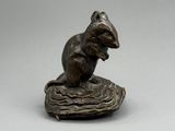 une statue en bronze représentant une souris assise sur un morceau de bois