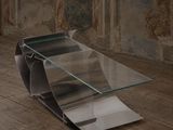 une table en verre avec un plateau incurvé, posée sur un parquet
