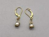 une paire de boucles d'oreilles en or et perles posées sur un fond gris