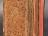 an old book sitting on top of a black table next to a red book