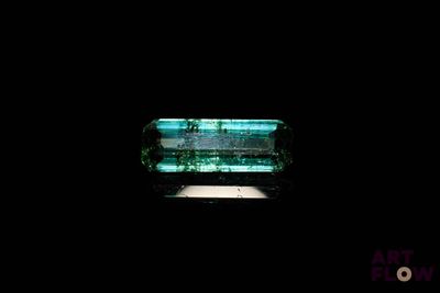une image représentant une bague en verre vert posée sur une surface noire