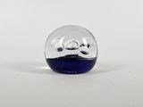 une petite boule de verre avec un socle bleu posée sur une surface blanche