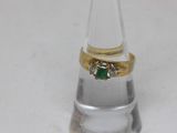 a gold ring with a green stone on top of a clear glass