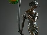 a bronze statue of a woman holding a flower and a lamp
