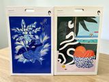 two paintings of flowers and fruit on display on the table