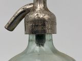 a green glass bottle with a metal handle on a table