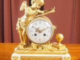 une horloge en or ornée d'un ange, posée sur une table en bois