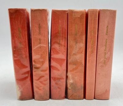 six livres rouges sont alignés sur une surface blanche