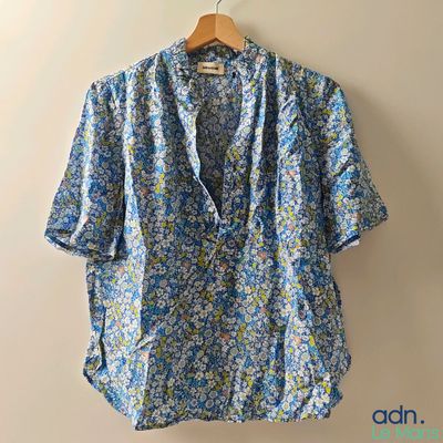 a blue floral shirt hanging on a hanger against a wall
