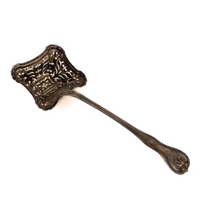une cuillère en argent ornée d'un motif élaboré, posée sur une surface blanche