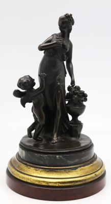 une statue antique en bronze représentant une femme et deux chiens, posée sur un socle en bois