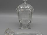 an antique glass jar with a spoon and spoon rest on a table