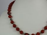 a close up of a necklace with red beads on a mannequin