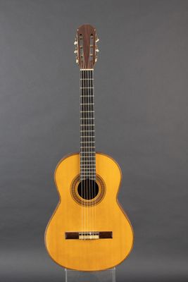 an acoustic guitar sitting on a stand against a gray background