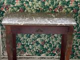 une petite table au plateau en marbre, placée devant un mur recouvert de papier peint