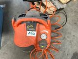 un compresseur d'air orange et noir posé sur le sol, à côté d'une pile de cartons