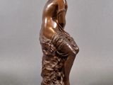 a bronze statue of a man sitting on a rock with his hands on his knees