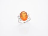 une bague sertie d'un saphir orange et de diamants, sur fond blanc