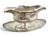 une saucière ancienne en argent posée sur un plateau, sur une surface blanche