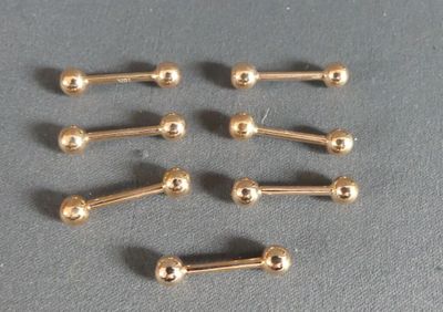 six pairs of gold plated nose studs on a gray surface