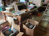 boxes of books are stacked on a table in a cluttered room