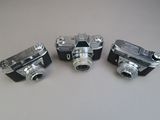 three old cameras are lined up on a white surface
