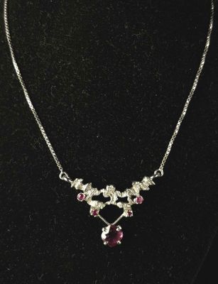 a silver necklace with pink stones on a black mannequin