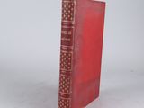 an old red book sitting on top of a table next to a white wall