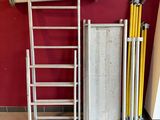 une échelle appuyée contre un mur rouge, à côté d'une pile d'échelles