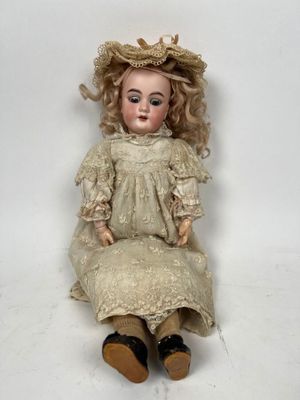 une poupée ancienne assise sur une surface blanche, vêtue d'une robe et d'un chapeau