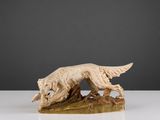 une statue représentant un chien assis sur une bûche, un oiseau dans la gueule