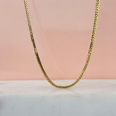 un collier à maillons dorés sur fond rose