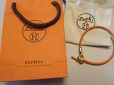 un sac Hermès orange orné d'une breloque dorée et d'un bracelet en cuir marron