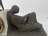 statue of a man sitting on a bench with a clock in front of him